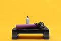 Step platform, mat, bottle of water and abdominal wheel on yellow. Sports equipment