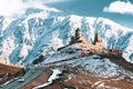 Stepantsminda, Georgia. Famous Gergeti Trinity Tsminda Sameba Church In Early Winter Landscape. Suv Moving Near Church