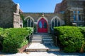Steps Leading Up to the Red Door of a Cobblestone Church With Trimmed Bushes on Each Side Royalty Free Stock Photo