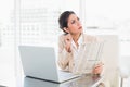 Stern businesswoman holding newspaper while working on laptop lo Royalty Free Stock Photo