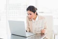 Stern businesswoman holding newspaper while working on laptop Royalty Free Stock Photo