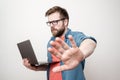 Stern man holds a laptop in one hand, and puts the other forward showing a stop gesture and looks sternly at the camera Royalty Free Stock Photo