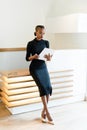 Stern elegant business woman wearing black dress and beige shoes in light office looking at her agenda, full length portrait Royalty Free Stock Photo