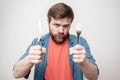 Stern, hungry bearded man holds a knife with a fork in his hands and looks angrily. Concept of diet, crisis or saving Royalty Free Stock Photo