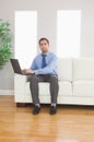 Stern young businessman using his laptop while sitting on cosy s