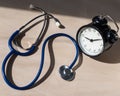 Stethoscope and alarm clock on a wooden table in the sunlight. A tool for measuring blood pressure. Desktop cardiologist