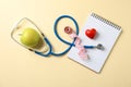 Stethoscope, apple, notebook, heart and measuring tape on yellow background