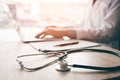 Stethoscope and background doctor using laptop at desk in clinic