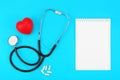 Stethoscope with blank notepad, red heart and white capsules on a blue background. Royalty Free Stock Photo