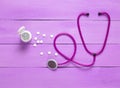 Stethoscope and bottle with pills on violet wooden background, medical concept, top view Royalty Free Stock Photo