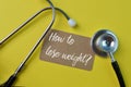 Stethoscope and brown card written with question HOW TO LOSE WEIGHT