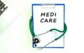 Stethoscope and clipboard with MEDI CARE text on white sheet of paper