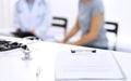 Stethoscope, clipboard with medical form lying on hospital reception desk with laptop computer and busy doctor and Royalty Free Stock Photo