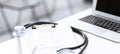 Stethoscope, clipboard with medical form lying on hospital reception desk with laptop computer and busy doctor and Royalty Free Stock Photo