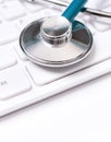 Stethoscope on computer keyboard on white background. Physician write medical case long term care treatment concept, close up, Royalty Free Stock Photo