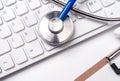 Stethoscope on computer keyboard on white background. Physician write medical case long term care treatment concept, close up, Royalty Free Stock Photo