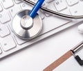 Stethoscope on computer keyboard on white background. Physician write medical case long term care treatment concept, close up, Royalty Free Stock Photo