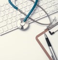 Stethoscope on computer keyboard on white background. Physician write medical case long term care treatment concept, top view, Royalty Free Stock Photo