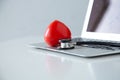 Stethoscope doctors and red heart placed on a white desk with laptop background hospital, concept: diagnostics disease health p