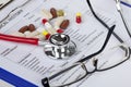 Stethoscope with eyeglasses and pills laying on a medical form