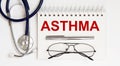 Stethoscope,glasses and pen with notepad with text asthma