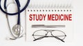 Stethoscope,glasses and pen with notepad with text STUDY MEDICINE