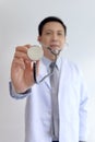 Stethoscope in hand of friendly smiling senior Asian male doctor in lab coat workwear on white wall of medical clinic, happy Royalty Free Stock Photo