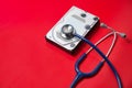 Stethoscope and hard disk drive on red background. Computer hardware diagnostic and repair concept Royalty Free Stock Photo