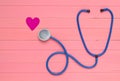 Stethoscope and heart on pastel pink wooden table. Cardiology equipment for diagnosing cardiovascular diseases. Top view.