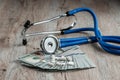 A stethoscope lies on a bundle of money and pills on a light wooden background. The concept of expensive medicine, medical