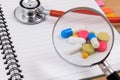 Stethoscope, magnify and many colorful pills on blank notepad. Royalty Free Stock Photo