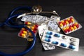stethoscope and medicines in different colored capsules on black background