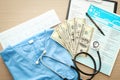 Stethoscope with money, laboratory tests and blue doctor's uniform on table