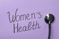 Stethoscope near text Women`s Health on violet background, top view