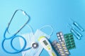 stethoscope, non-contact thermometer, protective masks and different medications on a blue background copy space top view