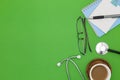 Stethoscope with notebook ,pen, white paper ,coffee cup,glasses, on green background,Medical background concept. Royalty Free Stock Photo