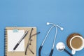 Stethoscope with notebook ,pencil, white paper ,coffee cup,glasses on blue background,Medical background concept. Royalty Free Stock Photo