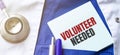 Stethoscope, pens and note with text VOLUNTEER NEEDED on the doctor uniform Royalty Free Stock Photo