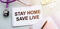 Stethoscope, pills and notebook with STAY HOME SAVE LIVE word on medical desk