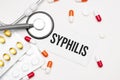 Stethoscope, pills and notebook with Syphilis word on medical desk