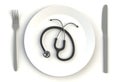 Stethoscope on plate, knife and fork on white table.