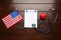 Stethoscope, red heart, clipboard and American flag on wooden table, flat lay Royalty Free Stock Photo