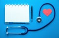 Stethoscope with red heart and notepad on blue background Royalty Free Stock Photo