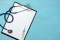 Stethoscope and syringe on clipboard with blank paper on blue wooden background Royalty Free Stock Photo