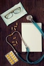 A stethoscope, thermometer, pills, notepad and pen on doctor table. Royalty Free Stock Photo