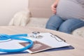 Stethoscope and ultrasound scan on the table, pregnant woman sitting on the sofa on the background Royalty Free Stock Photo