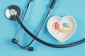 Stethoscope and various pills in a saucer in shape of heart on a blue wooden background Royalty Free Stock Photo