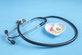 Stethoscope and various pills in a saucer in shape of heart on a blue wooden background Royalty Free Stock Photo