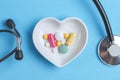 Stethoscope and various pills in a saucer in shape of heart on a blue wooden background Royalty Free Stock Photo