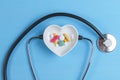 Stethoscope and various pills in a saucer in shape of heart on a blue wooden background Royalty Free Stock Photo